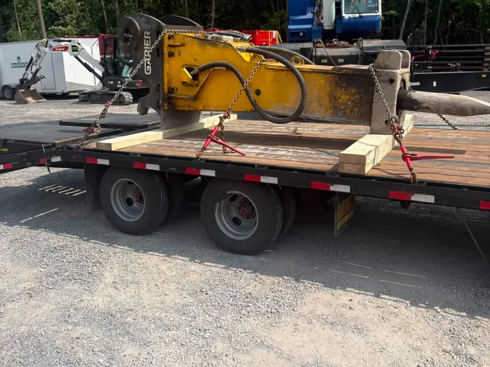 Marteau hydraulique arrimé sur une remorque plateau, prêt pour le transport